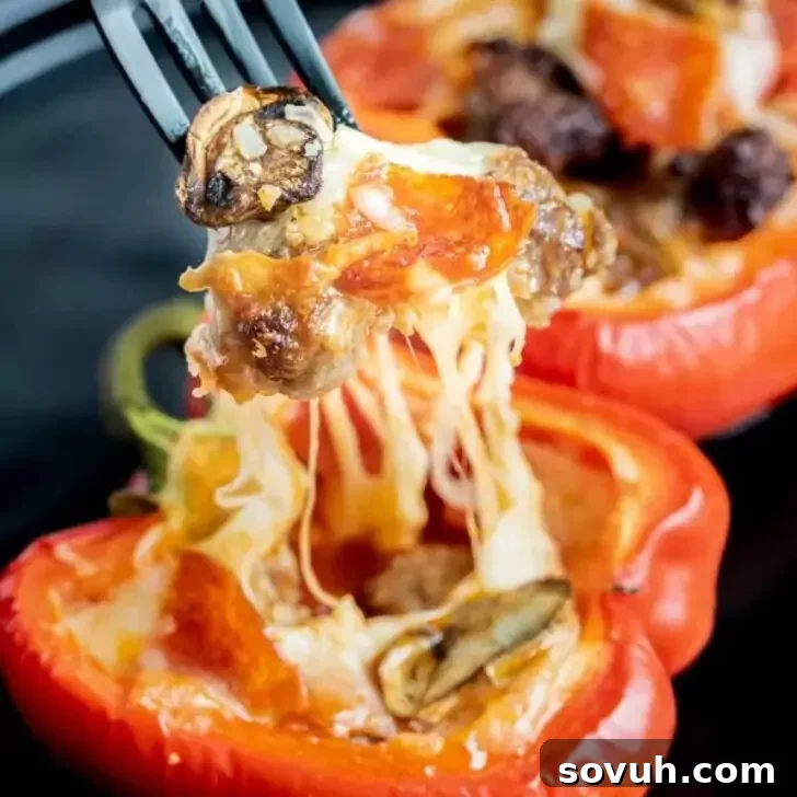 A fork lifting a cheesy stuffed red bell pepper filled with mushrooms, pepperoni, and Italian sausage, with another stuffed pepper in the background.