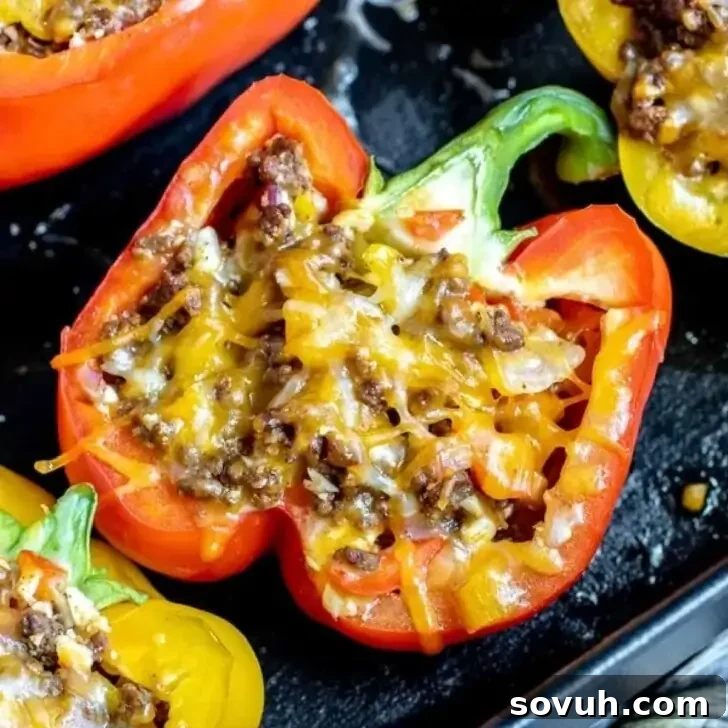 Halved bell peppers stuffed with a savory mixture of seasoned ground meat, onions, and melted cheese on a black tray, fresh out of the oven.