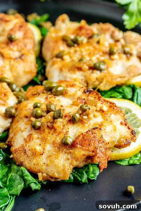 Plated Keto Chicken Piccata on a bed of fresh spinach, adorned with lemon wedges and a generous drizzle of the caper sauce.