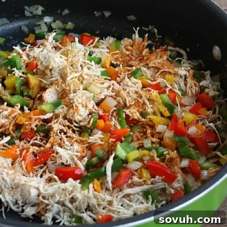 A vibrant mix of shredded chicken, diced red and green bell peppers, and onions simmering in a pan with taco seasoning.