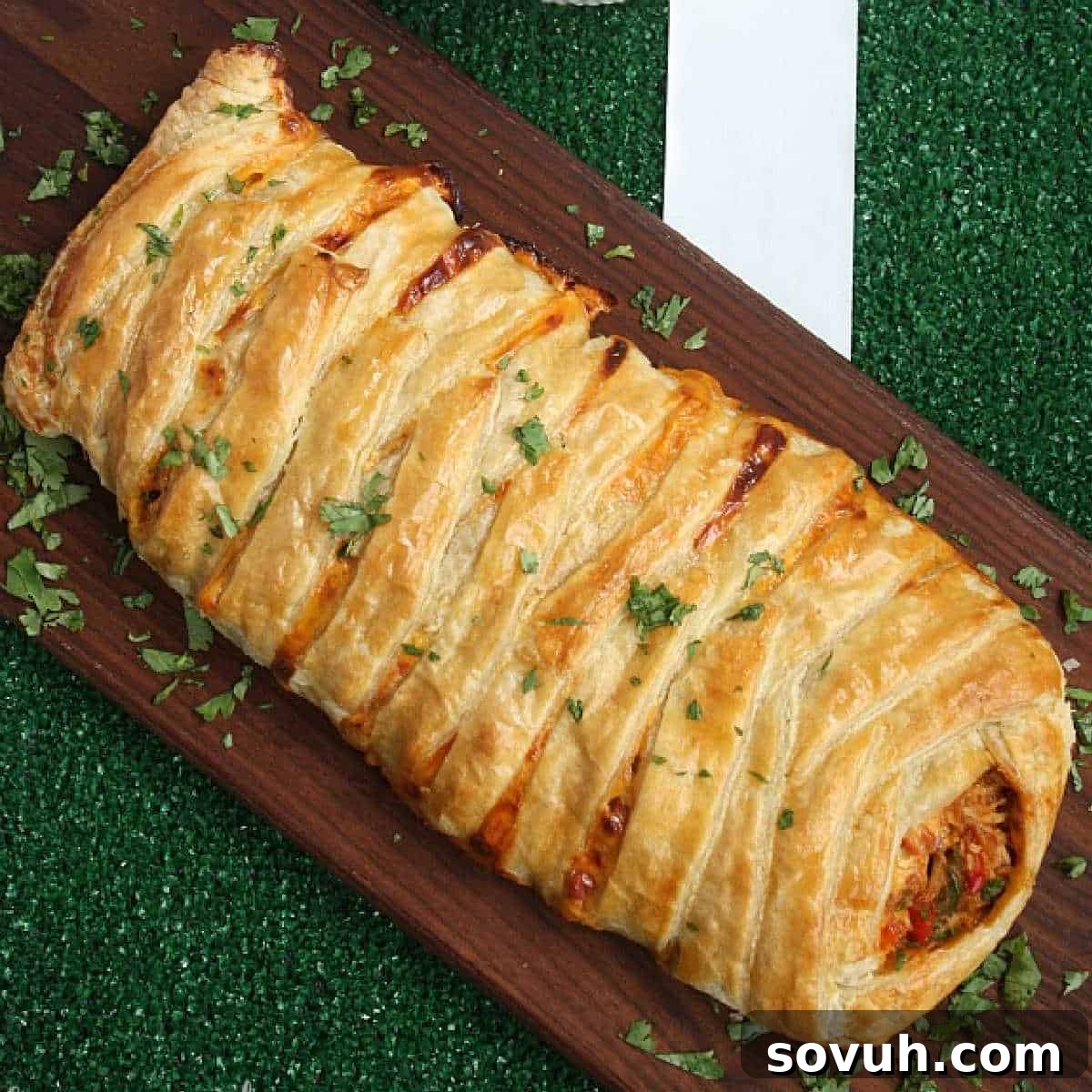 A freshly baked, golden-brown chicken taco braid on a wooden board, garnished with fresh cilantro, ready to be served.