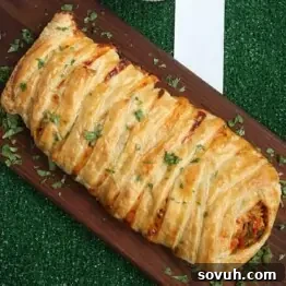 A vibrant, golden-brown chicken taco braid on a wooden board, garnished with fresh herbs, alongside a bowl of creamy cheese dip.