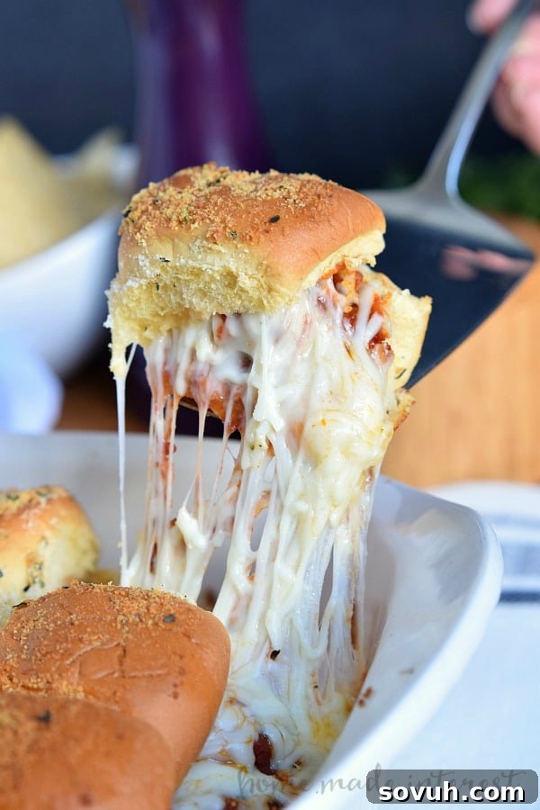 Close-up of a cheesy Meatball Slider being lifted, showcasing the melted cheese and soft bun.