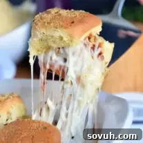 Cheesy meatball slider being lifted out of pan, showing melted cheese and bun.