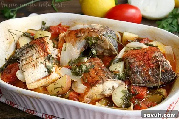 A close-up of Portuguese-style Baked Rockfish, perfectly cooked and flaky, served directly in the baking dish. The golden-brown fish is surrounded by tender potatoes and juicy tomatoes, garnished with fresh parsley. This healthy and simple seafood dish is ready to be enjoyed.
