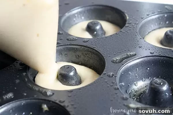 Filling a mini donut pan with lemon poppy seed batter using a piping bag, ensuring perfect shapes.