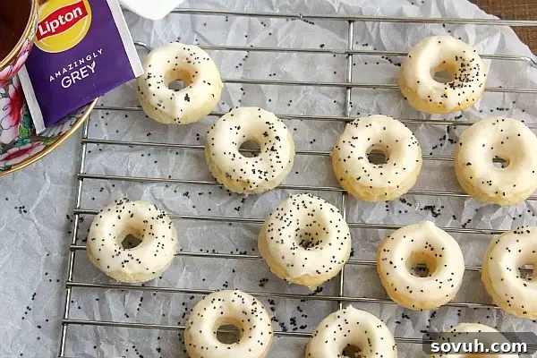 Mini lemon poppy seed donuts cooling on a wire rack, freshly glazed and sprinkled with poppy seeds.