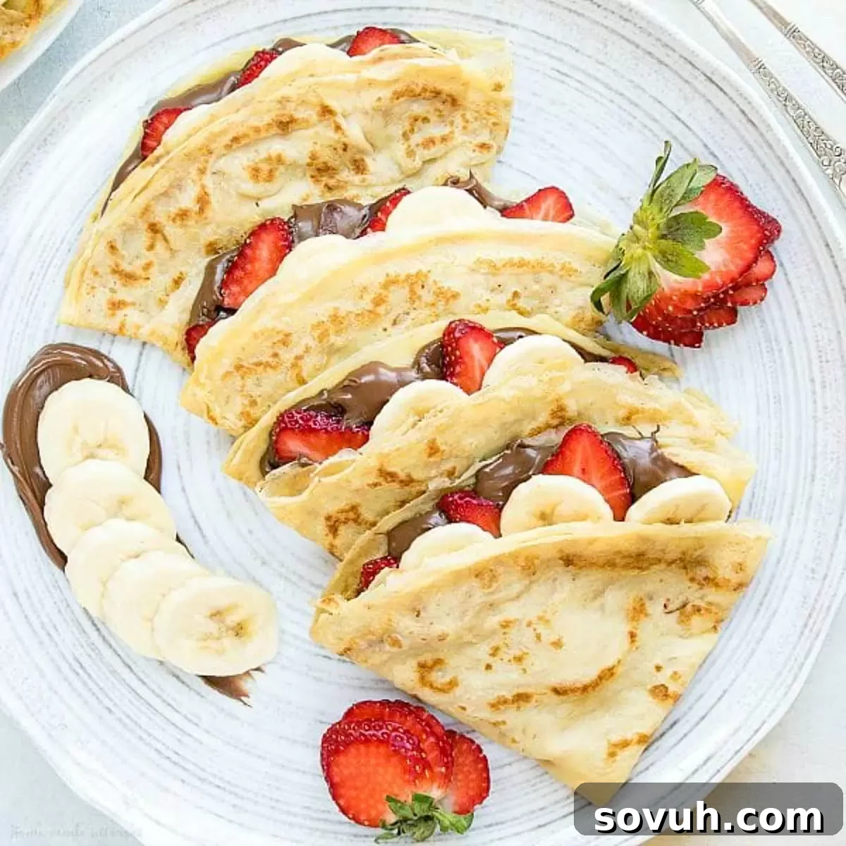 Homemade Crepes with rich Nutella Hazelnut Spread and fresh berries on a white plate.