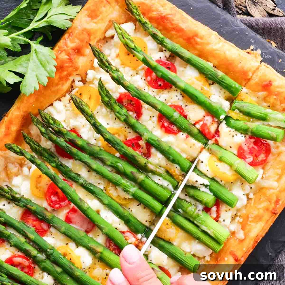 A stunning Asparagus Puff Pastry Tart with goat cheese and tomatoes, being sliced.