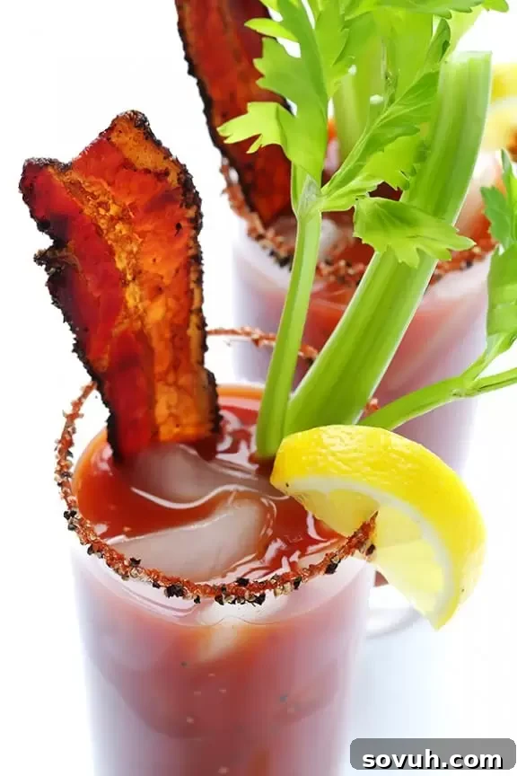 A vibrant Peppered Bacon Bloody Mary, garnished with crispy bacon, fresh herbs, and a lemon wedge.