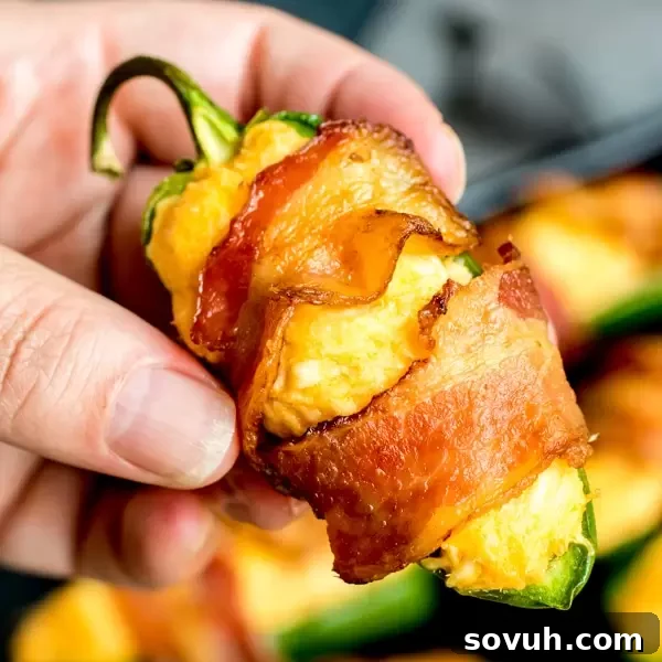 Hand holding a crispy Buffalo Chicken Jalapeno Popper, showcasing its cheesy filling and bacon wrap