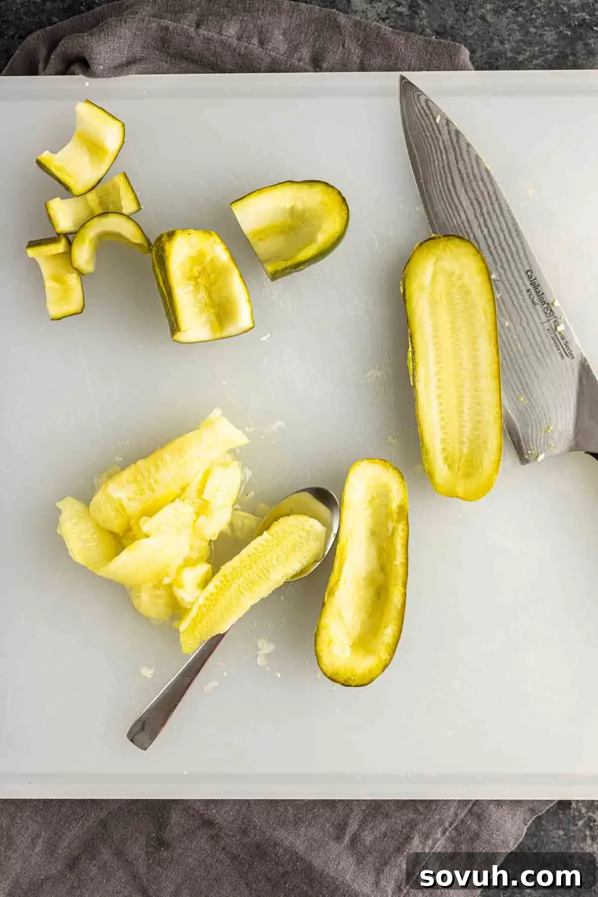 The Devil's Own Pickles 4 A wooden cutting board displays a sharp chef's knife alongside the key components for making deviled pickle appetizers. A whole pickle is shown being carefully hollowed out with a small spoon, demonstrating the preparation step. Nearby are pieces of sliced pickles with their insides scooped out, perfectly prepped to be filled. This image illustrates the essential technique for creating unique twists on classic deviled eggs, focusing on pickle-based recipes.
