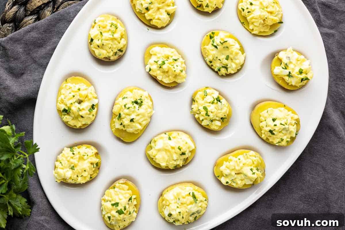 Zesty Potato Morsels 2 A white oval platter displays halved potatoes filled with a creamy, yellow egg salad mixture, garnished with chopped herbs—perfect party potato bites inspired by a classic deviled potato recipe.