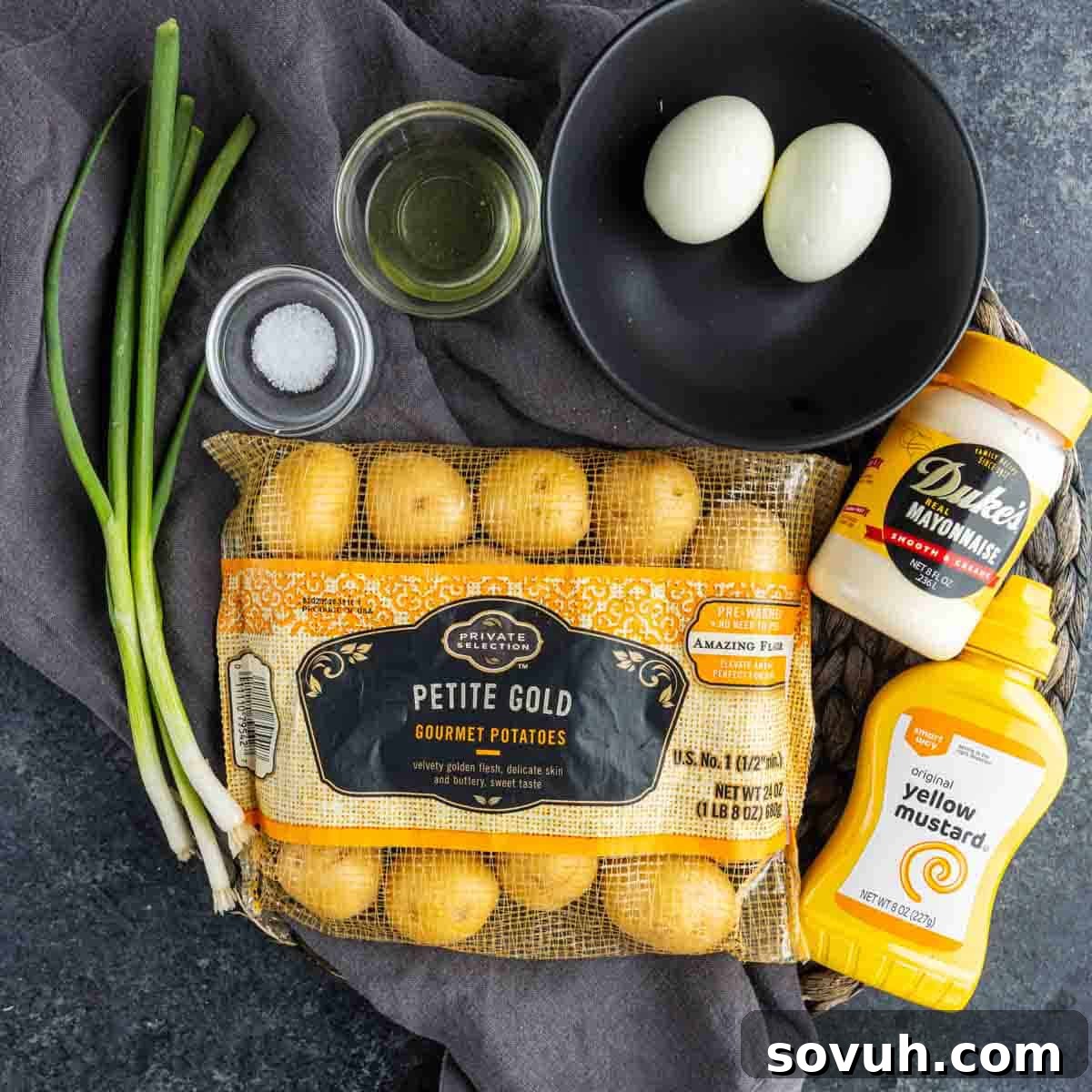 Zesty Potato Morsels 3 A bag of petite gold potatoes, two boiled eggs in a bowl, green onions, mayo, mustard, salt, and oil—everything you need for deviled potatoes or an easy potato appetizer perfect for party potato bites on a gray cloth.