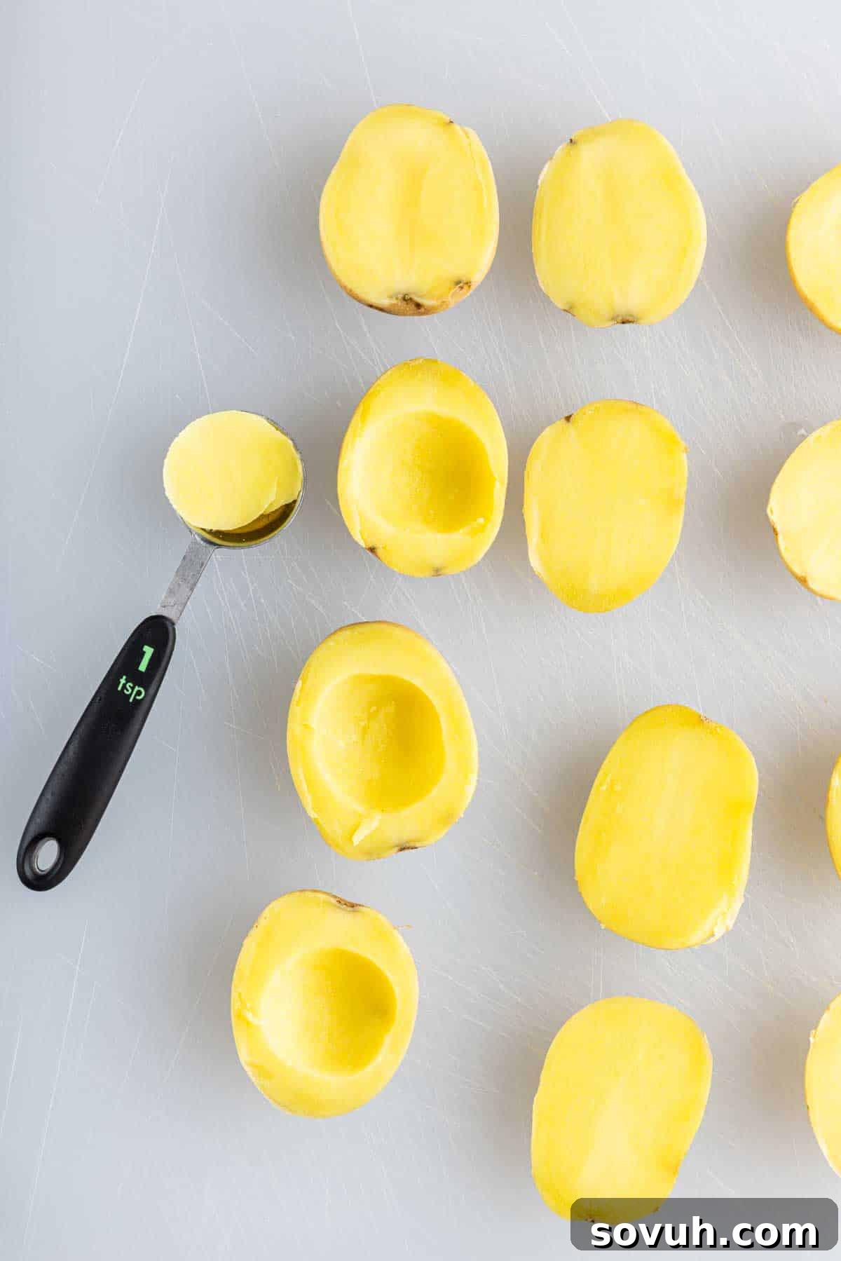 Zesty Potato Morsels 4 Several yellow potato halves are shown on a white surface, some hollowed out with a melon baller labeled "1 tsp," ready to be filled for a tasty deviled potato recipe or served as party potato bites.