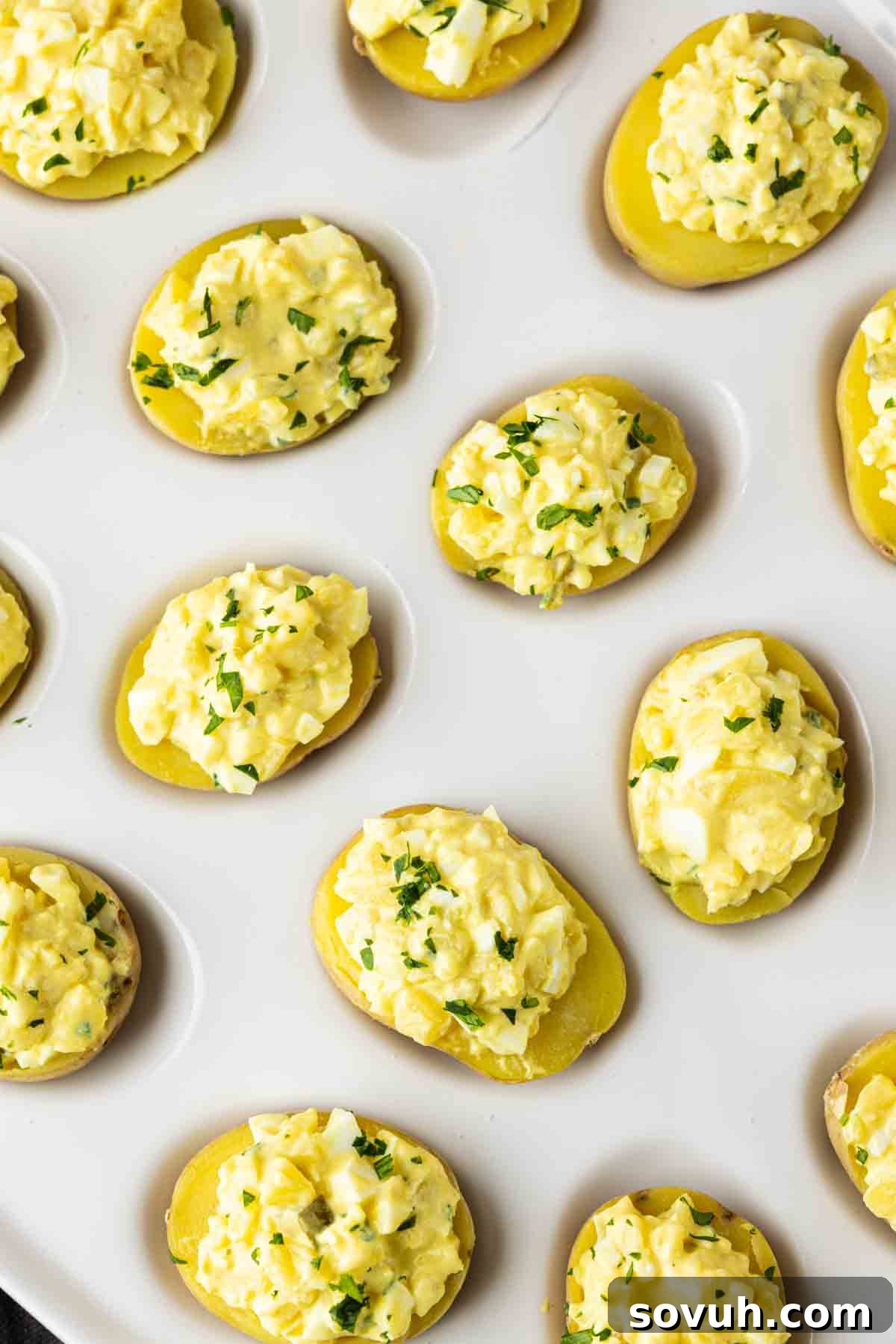 Zesty Potato Morsels 5 Halved potatoes topped with a yellow egg salad mixture and chopped herbs, these party potato bites make an easy potato appetizer, perfectly arranged on a white surface.
