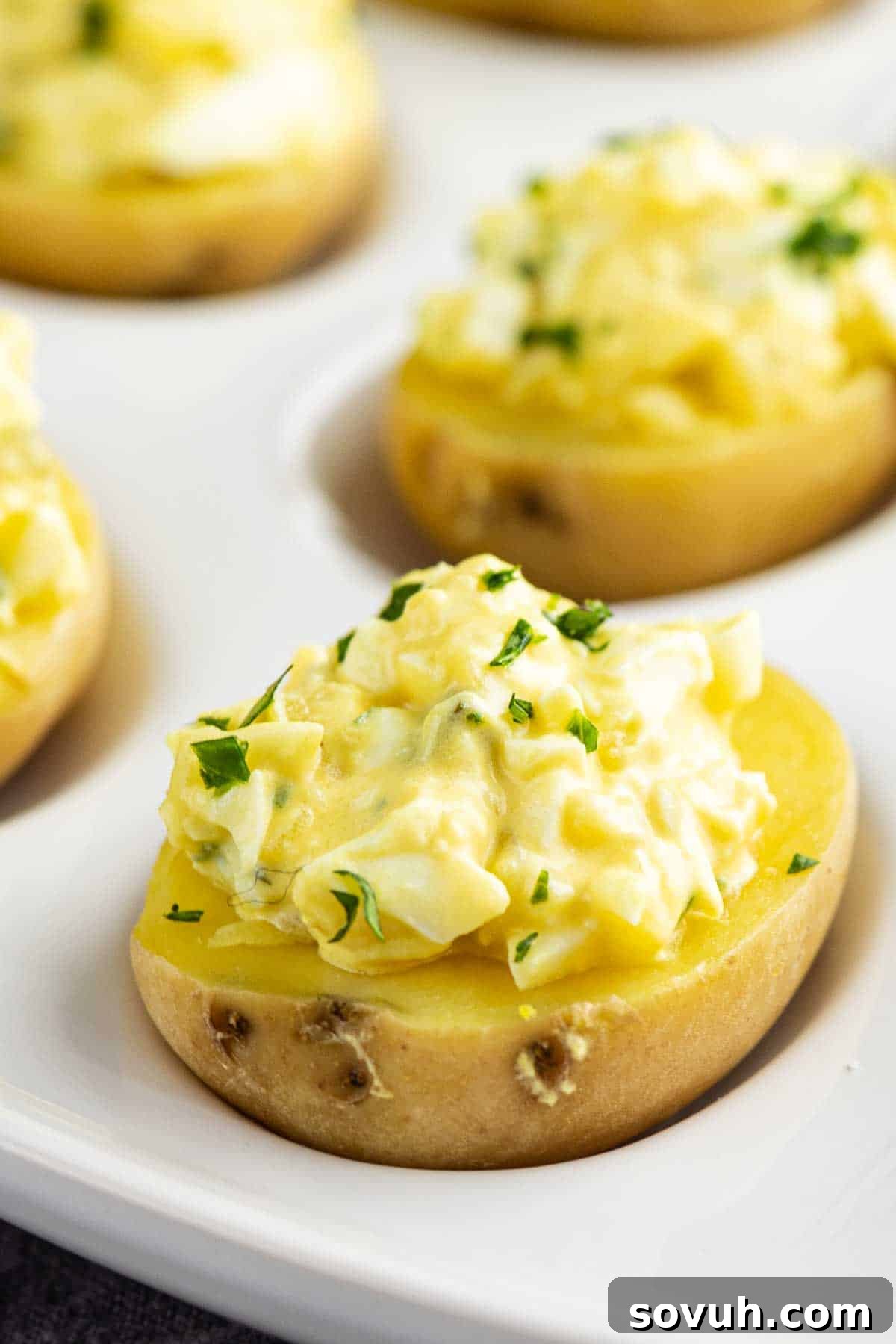 Zesty Potato Morsels 6 Halved small potatoes topped with creamy egg salad and parsley, these party potato bites are arranged on a white serving tray—an irresistible deviled potato recipe perfect for any gathering.
