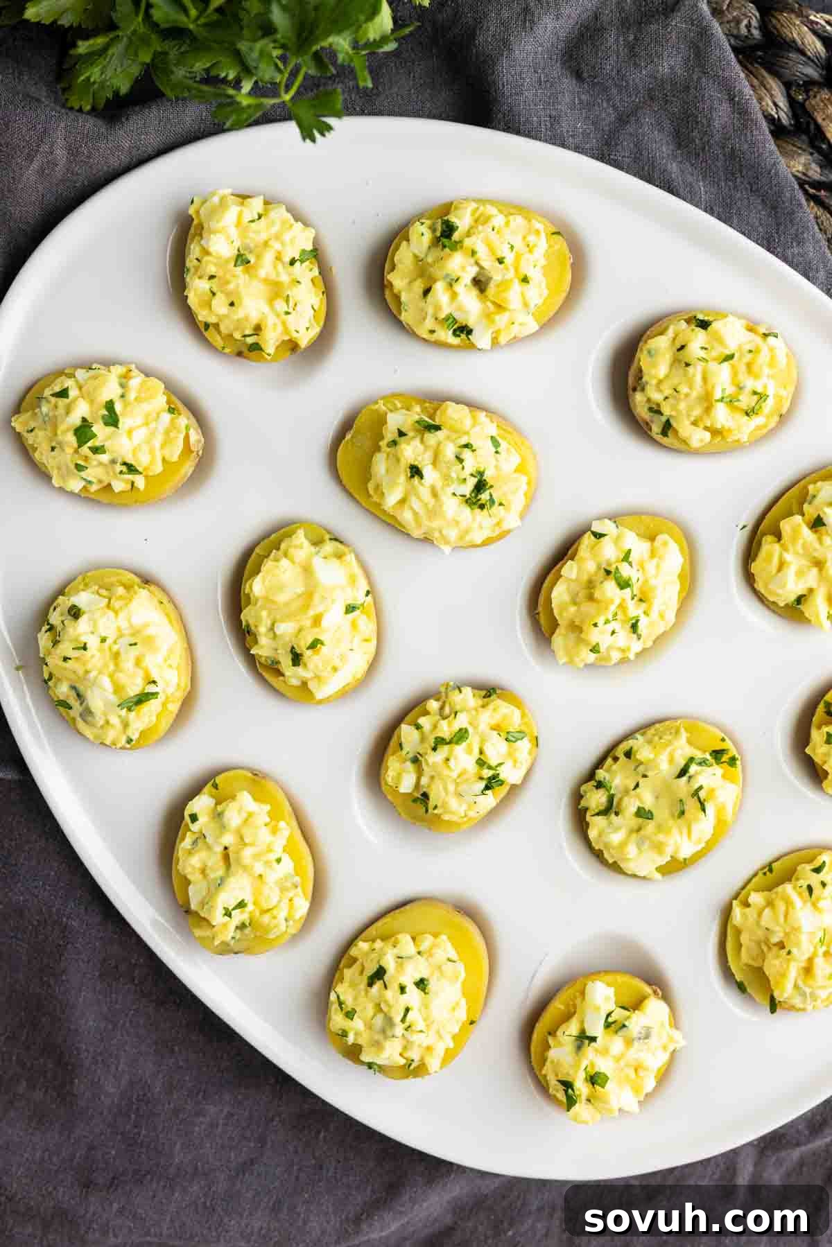 Zesty Potato Morsels 7 A white plate with several halved boiled potatoes topped with a yellow egg salad mixture and garnished with chopped herbs, making these party potato bites an easy potato appetizer for any gathering.