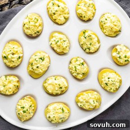 A white platter with several deviled eggs topped with a chopped egg mixture and garnished with green herbs.