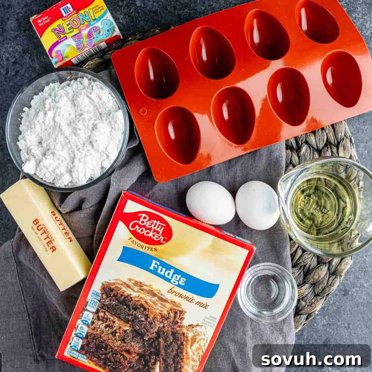 Devilish Easter Brownies from a Box 3 Brownie mix, butter, eggs, oil, water, powdered sugar, neon food coloring, and a red silicone egg-shaped mold arranged on a counter for easy Easter dessert Deviled Brownies.