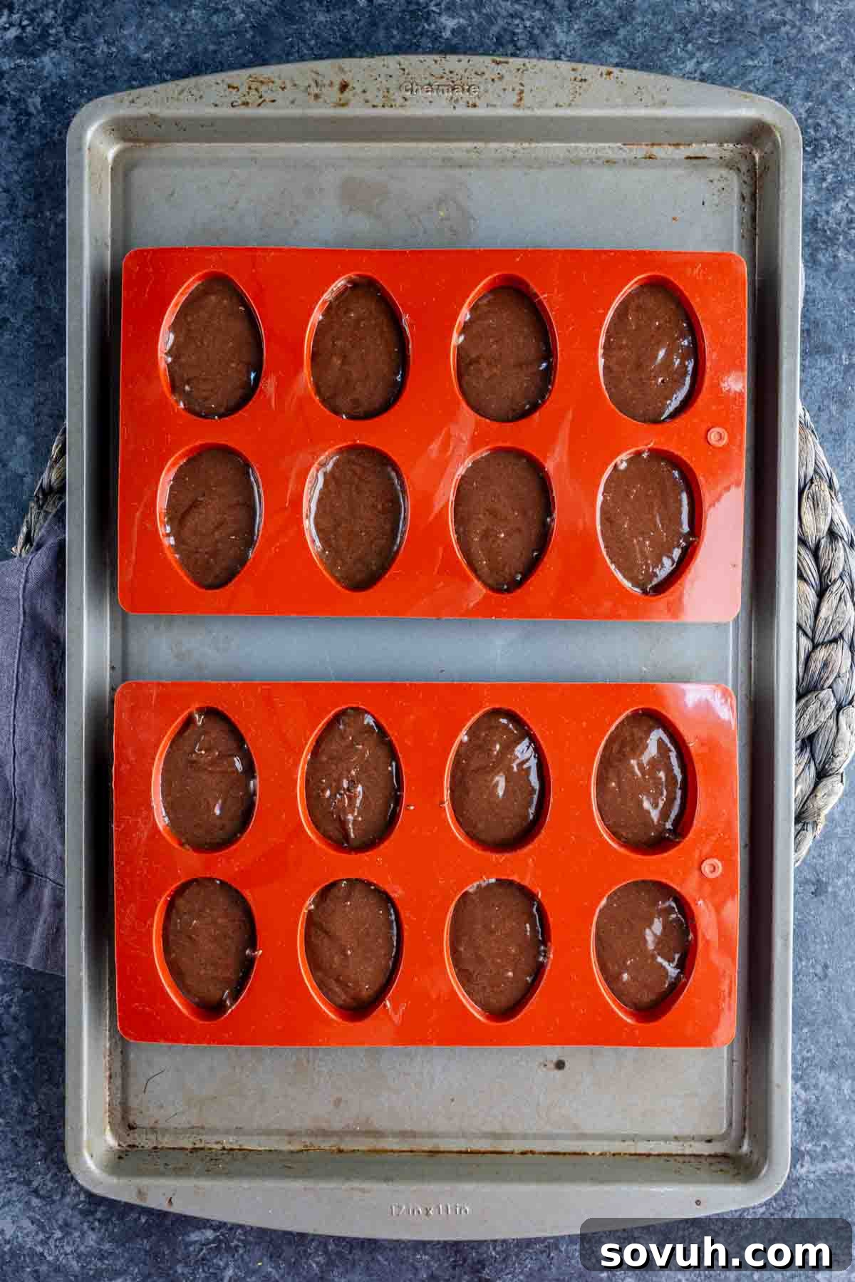 Devilish Easter Brownies from a Box 4 Two orange silicone egg molds filled with chocolate batter sit on a metal baking sheet, ready to become festive Easter brownies.