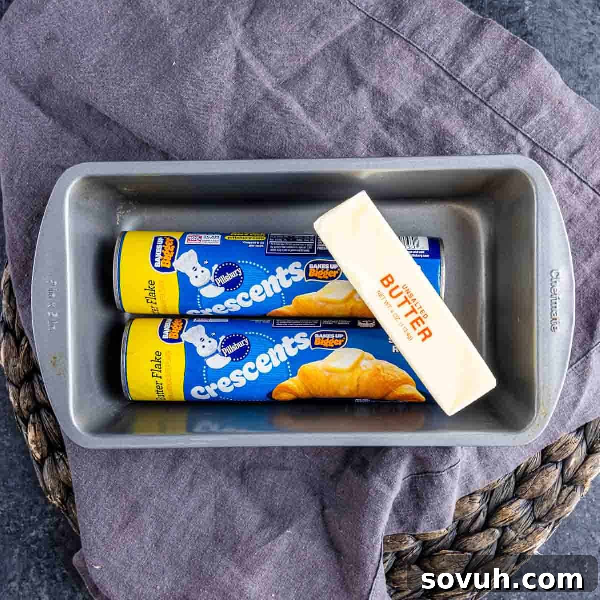 The Viral Golden Crescent Bake 3 A metal baking pan contains two cans of Pillsbury crescent rolls and a stick of butter, ready to be transformed into a delicious loaf.