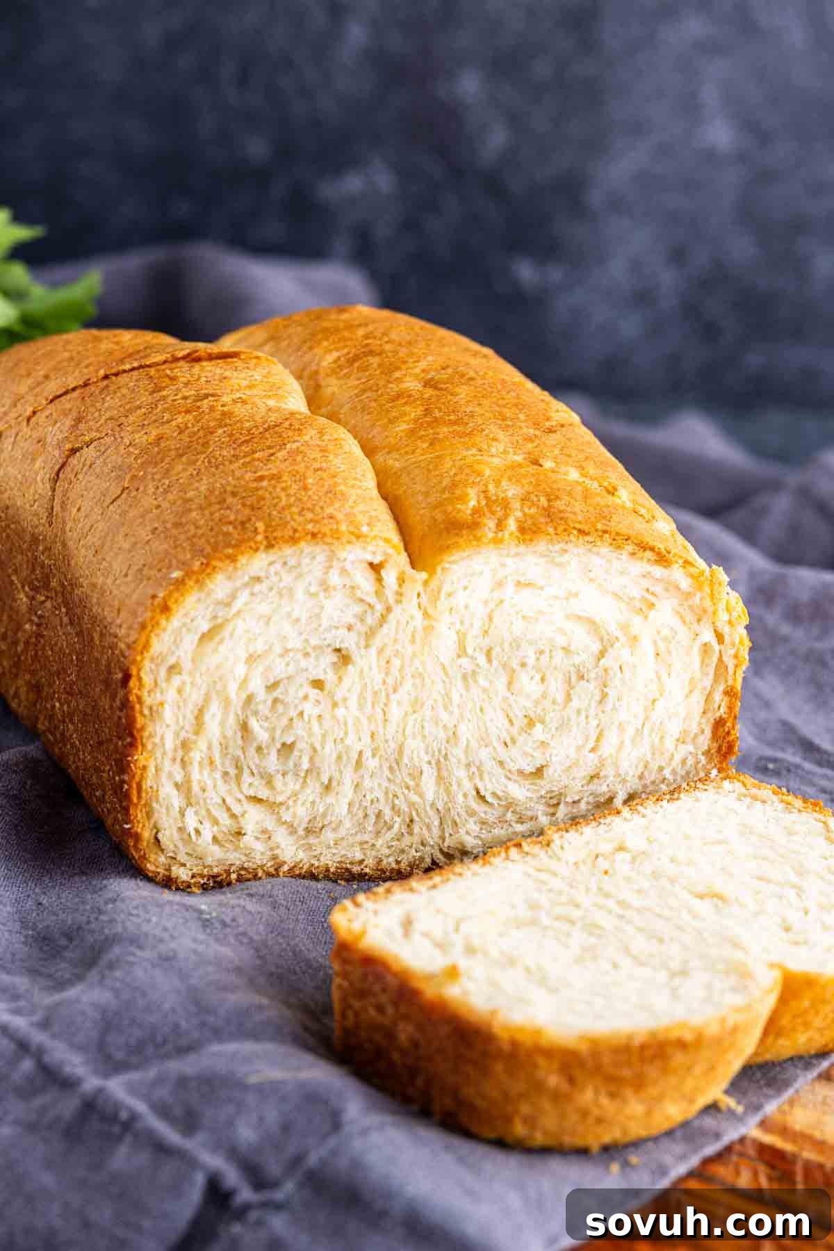 The Viral Golden Crescent Bake 6 A loaf of freshly baked, buttery bread loaf with a golden brown crust, partially sliced and resting on a gray cloth, ready to be served.
