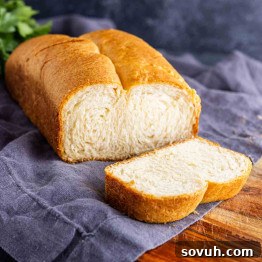 The Viral Golden Crescent Bake 8 A loaf of white bread with a single slice cut, placed on a gray cloth on a wooden surface.
