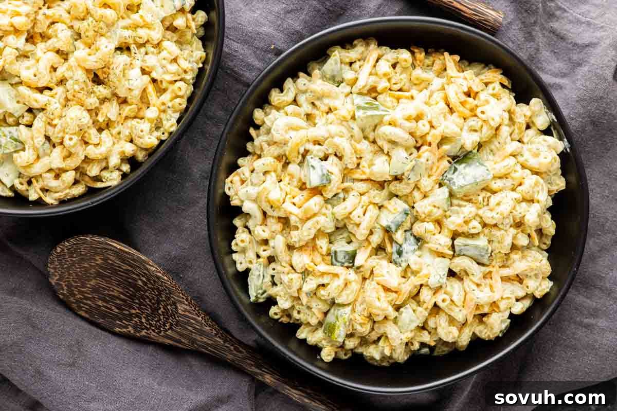 Quick and Zesty Dill Pickle Pasta Salad 2 Two black bowls brimming with creamy Dill Pickle Pasta Salad, featuring elbow pasta, vibrant chopped dill pickles, and a rich, light green dressing. The bowls rest on a dark linen cloth, flanked by wooden serving utensils, highlighting this easy and delicious make-ahead side dish for any gathering.