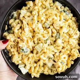 A hand holds a black bowl filled with macaroni salad mixed with diced vegetables and a creamy dressing.