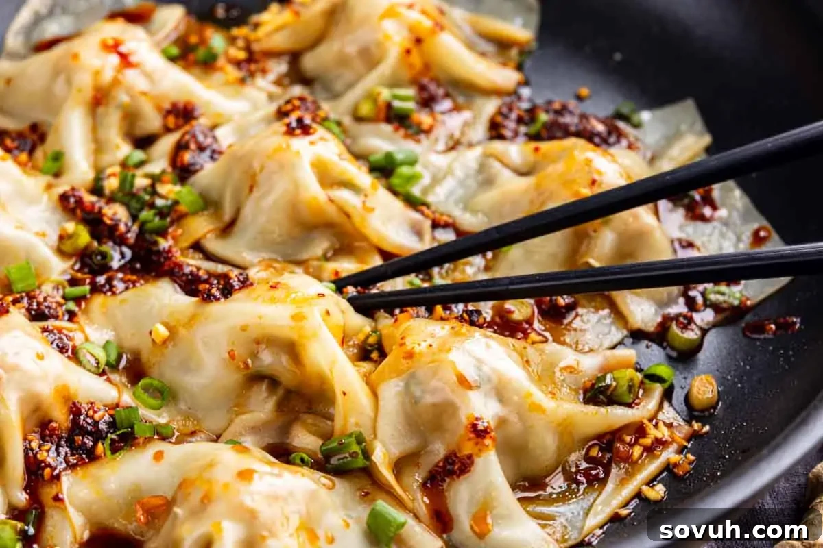Effortless Viral Blanket Dumplings No Folding Needed 2 Black chopsticks hold a pork dumpling topped with chili oil and chopped green onions, with several more no fold dumplings in sauce visible in a skillet.