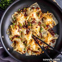 Effortless Viral Blanket Dumplings No Folding Needed 11 A black pan filled with cooked dumplings topped with chili oil and chopped green onions, with black chopsticks picking up one dumpling.