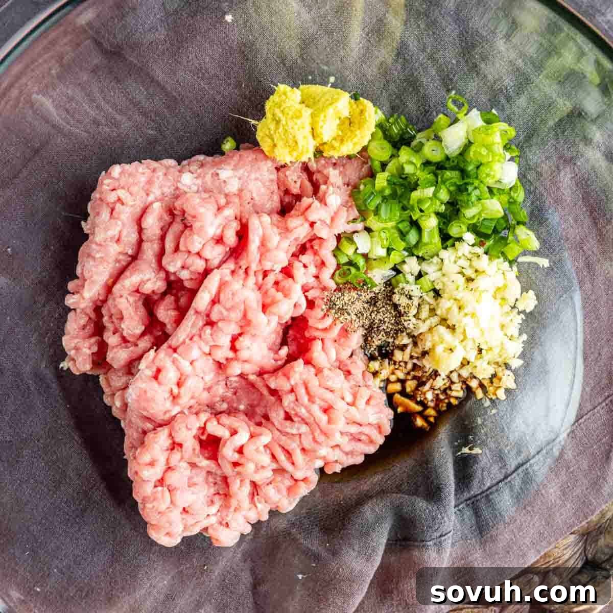 Effortless Viral Blanket Dumplings No Folding Needed 4 A glass bowl containing ground meat, chopped green onions, minced garlic, grated ginger, black pepper, and a dark sauce—perfect for making viral TikTok dumplings.