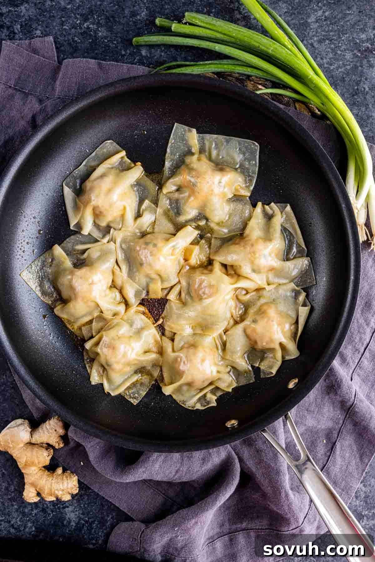 Effortless Viral Blanket Dumplings No Folding Needed 8 A black skillet with eight golden pork dumplings, inspired by viral TikTok dumplings, sits on a dark cloth, with fresh ginger and green onions nearby.