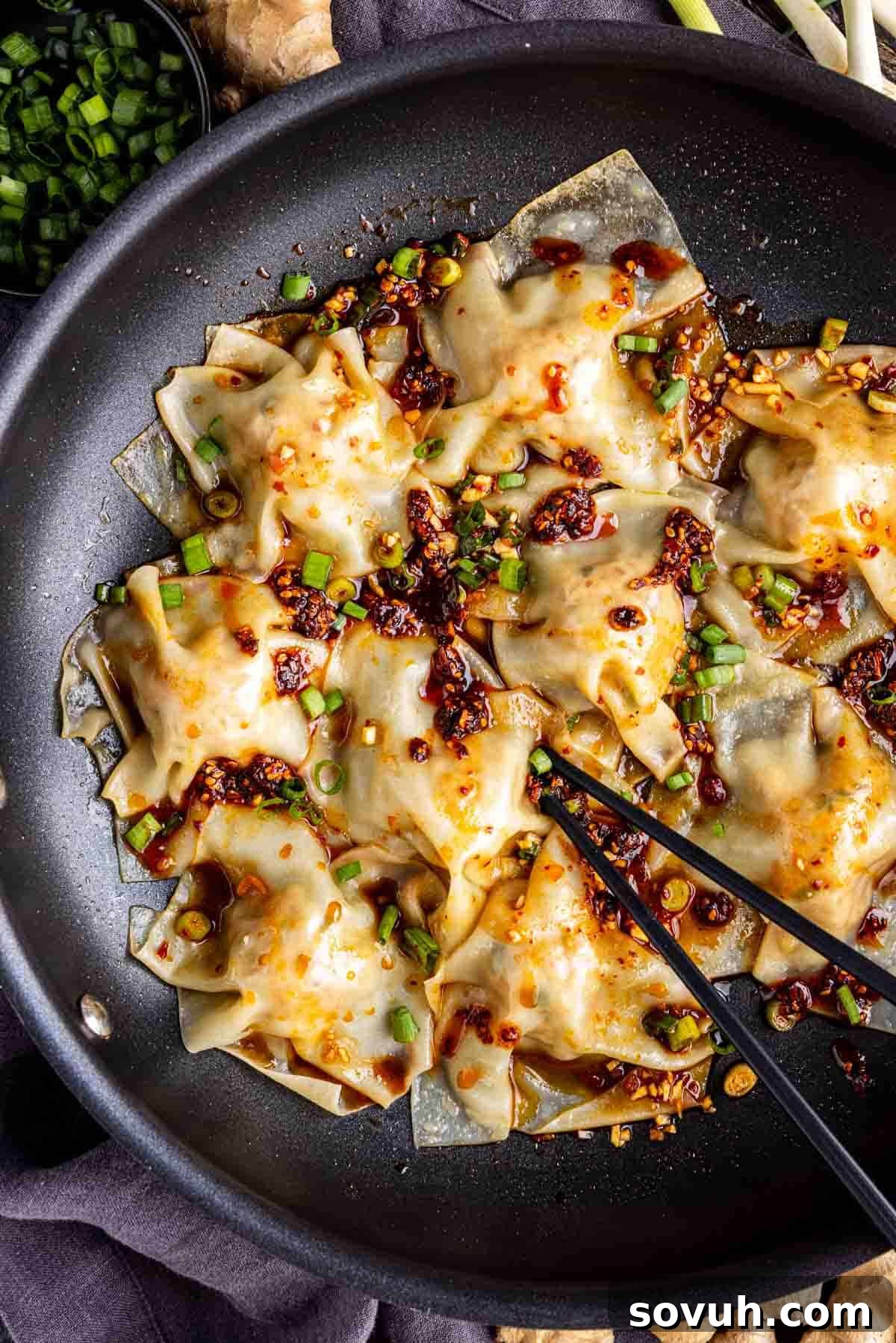 Effortless Viral Blanket Dumplings No Folding Needed 9 Pan-fried pork dumplings topped with chopped green onions and chili oil, served in a black skillet with chopsticks—these viral blanket dumplings are perfect for sharing.