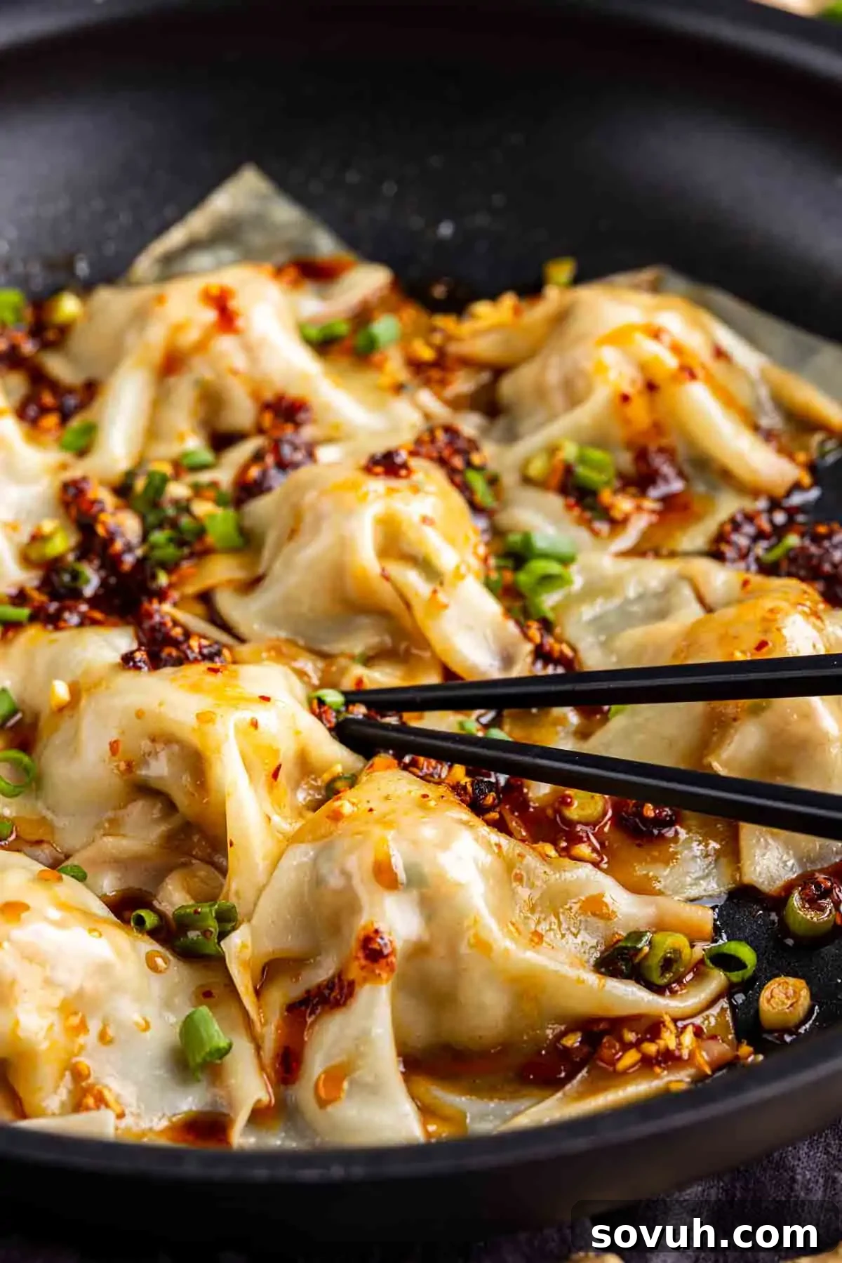 Effortless Viral Blanket Dumplings No Folding Needed 10 A close-up of no fold dumplings, topped with chili oil and chopped green onions in a black pan, with a pair of chopsticks picking up one TikTok dumpling.