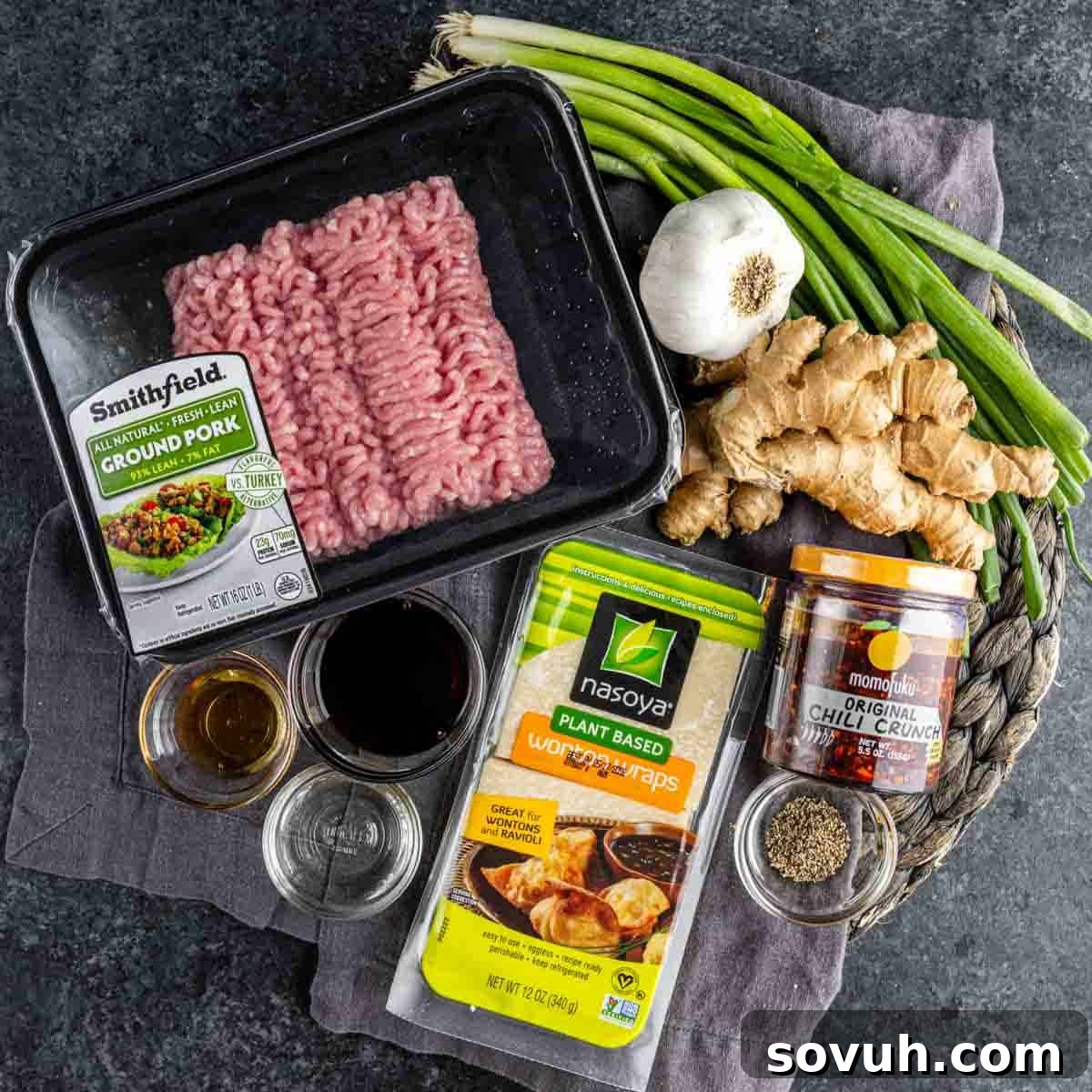 Viral Wonton Lasagna Twist 3 Ingredients for wonton wrapper dumplings, including ground pork, soy sauce, garlic, ginger, green onions, chili crunch, black pepper, and sesame oil, arranged on a dark surface—perfect for creating viral dumpling lasagna.