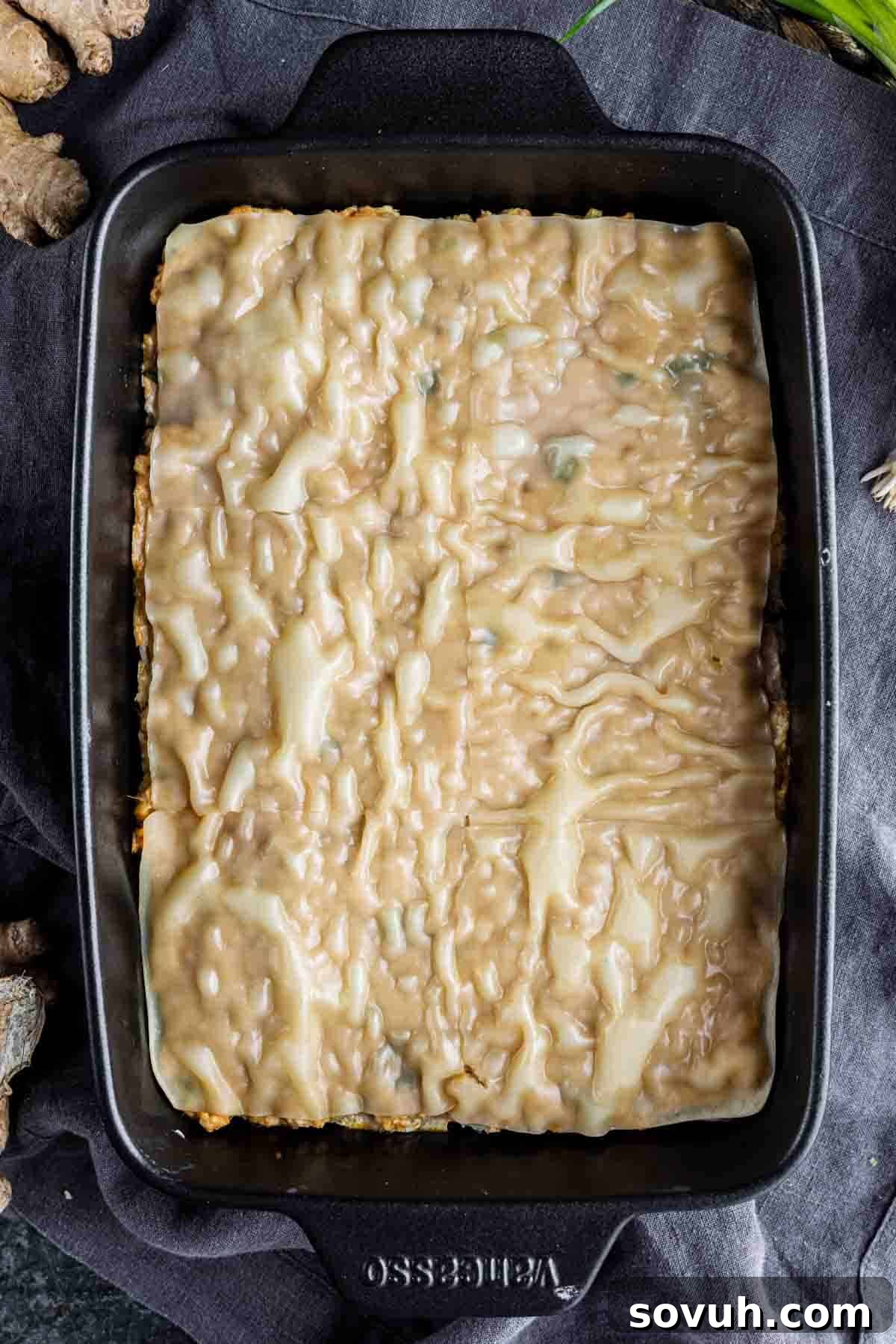 Viral Wonton Lasagna Twist 9 Rectangular baking dish with an unbaked viral dumpling lasagna topped with an even layer of creamy sauce, placed on a dark cloth.