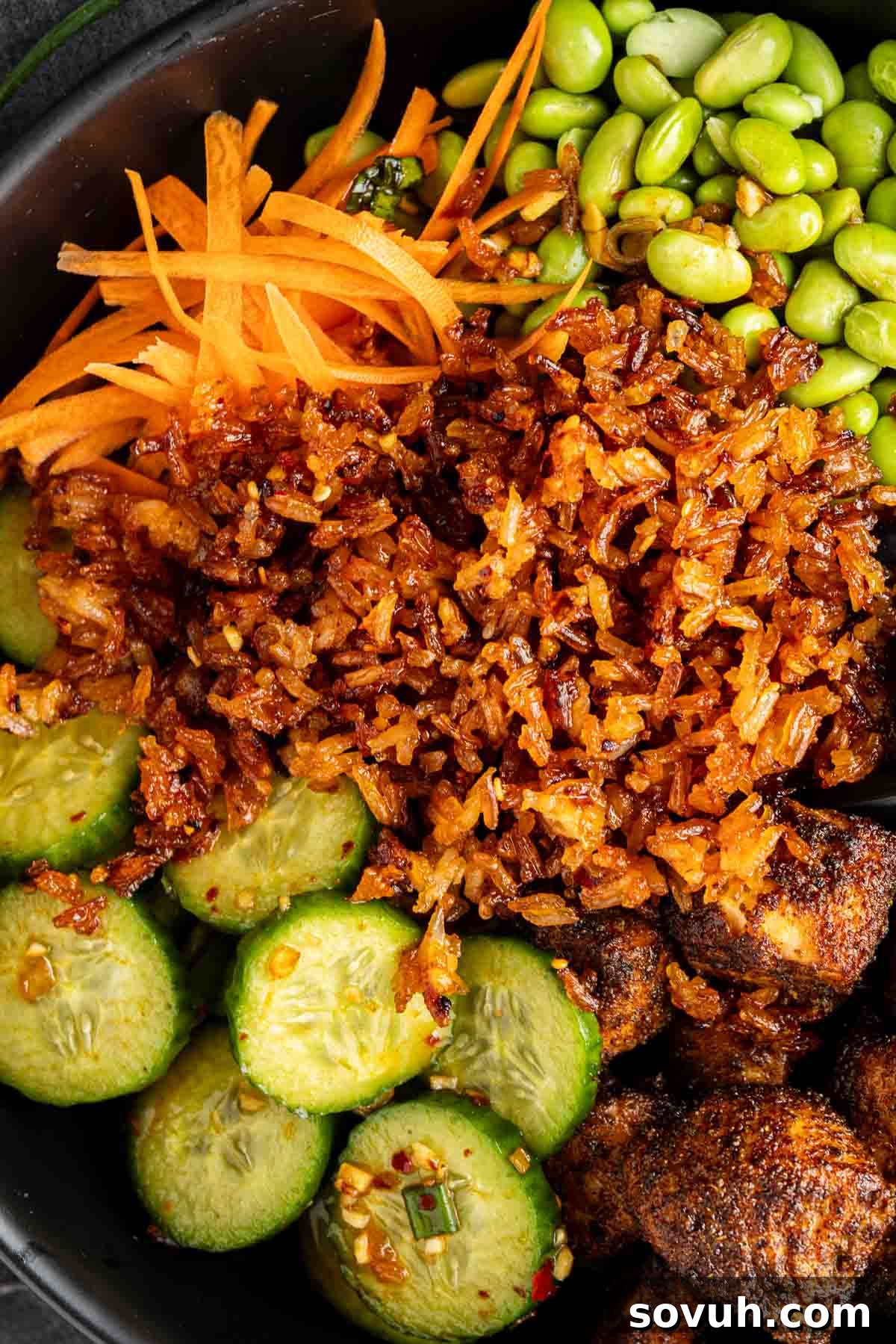 A close-up of a delicious crispy rice bowl featuring shredded carrots, edamame, sliced cucumbers, and seasoned mushrooms atop a bed of golden crispy rice.