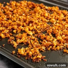 Golden-brown, crispy rice spread out on a dark baking sheet, showing an even layer of small, toasted grains—perfect for your next crispy rice bowl or to inspire a new crispy rice recipe.