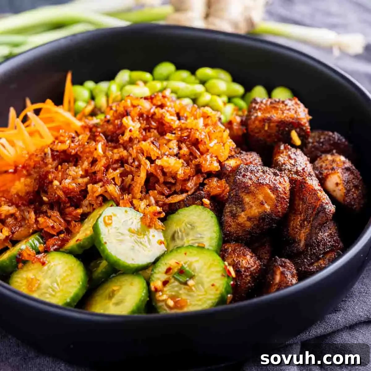 Chili Crisp Salmon Crispy Rice Bowl 4 A close-up of a vibrant Salmon Crispy Rice Bowl, showcasing individual components artfully arranged. The bowl contains perfectly cooked salmon bites, crisp golden rice, thinly sliced cucumbers, brightly shredded carrots, and tender green edamame. A generous drizzle of rich, red chili crisp dressing cascades over the ingredients, promising a burst of flavor and texture in every spoonful.