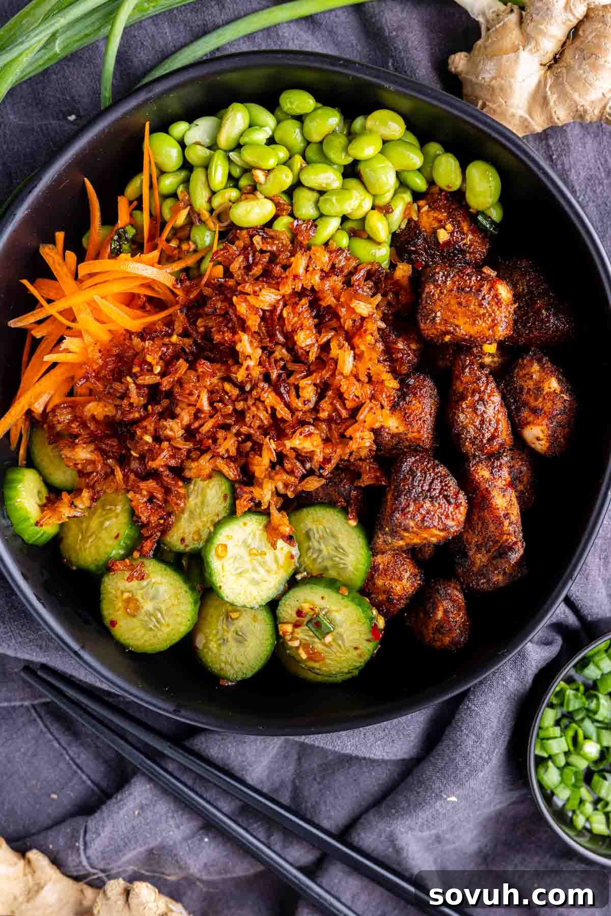 Chili Crisp Salmon Crispy Rice Bowl 5 A vibrant, neatly sectioned bowl of cooked rice, perfectly cubed seasoned salmon, crisp sliced cucumber, bright shredded carrots, and tender edamame, designed like a gourmet meal prep salmon bowl. A pair of elegant black chopsticks rests invitingly beside the bowl, hinting at an Asian-inspired delight. This dish is expertly prepared and ideal for pairing with a spicy chili crisp dressing for an extra kick of flavor.