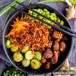 Chili Crisp Salmon Crispy Rice Bowl 6 A vibrant Salmon Crispy Rice Bowl filled with cooked tofu, shredded carrots, sliced cucumbers, edamame, and rice, garnished with chopped green onions and black chopsticks resting on top.