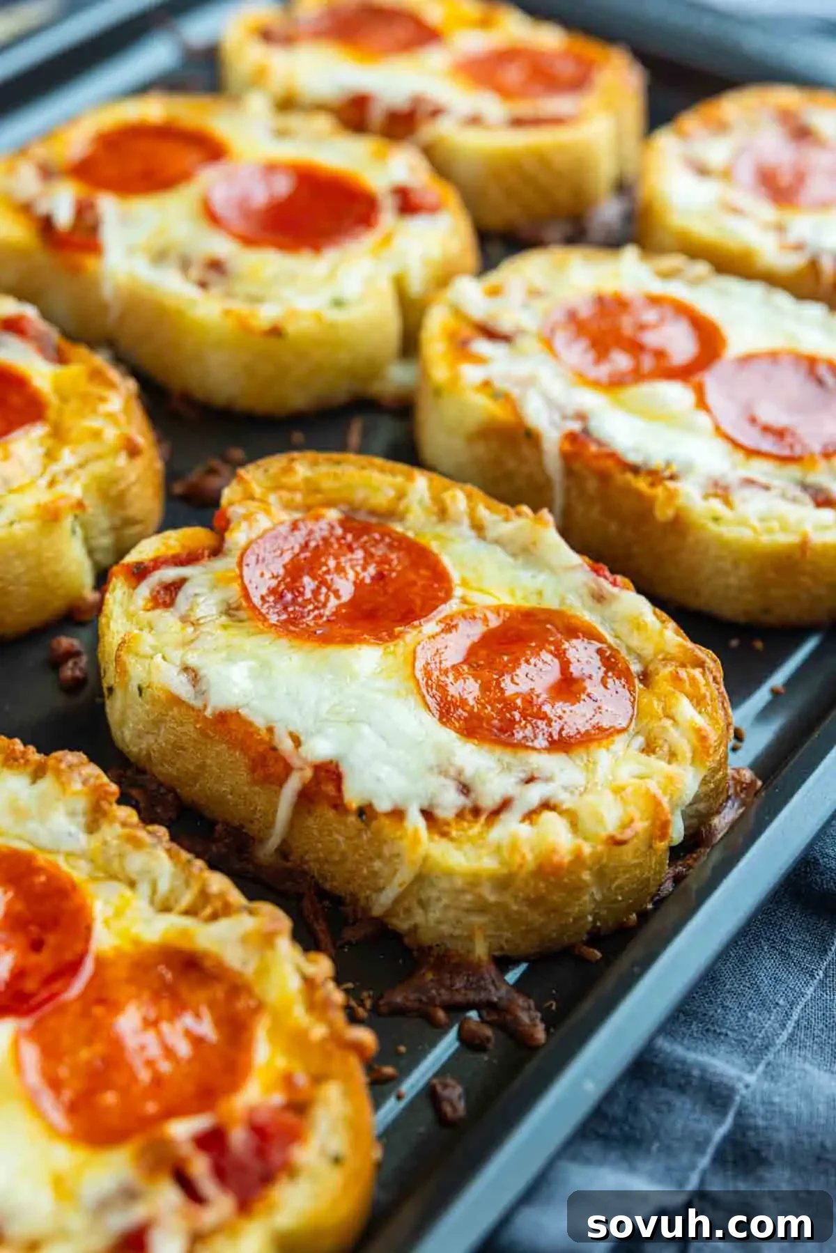 15-Minute Texas Toast Pizza Recipe for Quick Family Dinner 7 Slices of bread topped with melted cheese, tomato sauce, and pepperoni are arranged on a baking sheet for an easy pizza toast recipe.