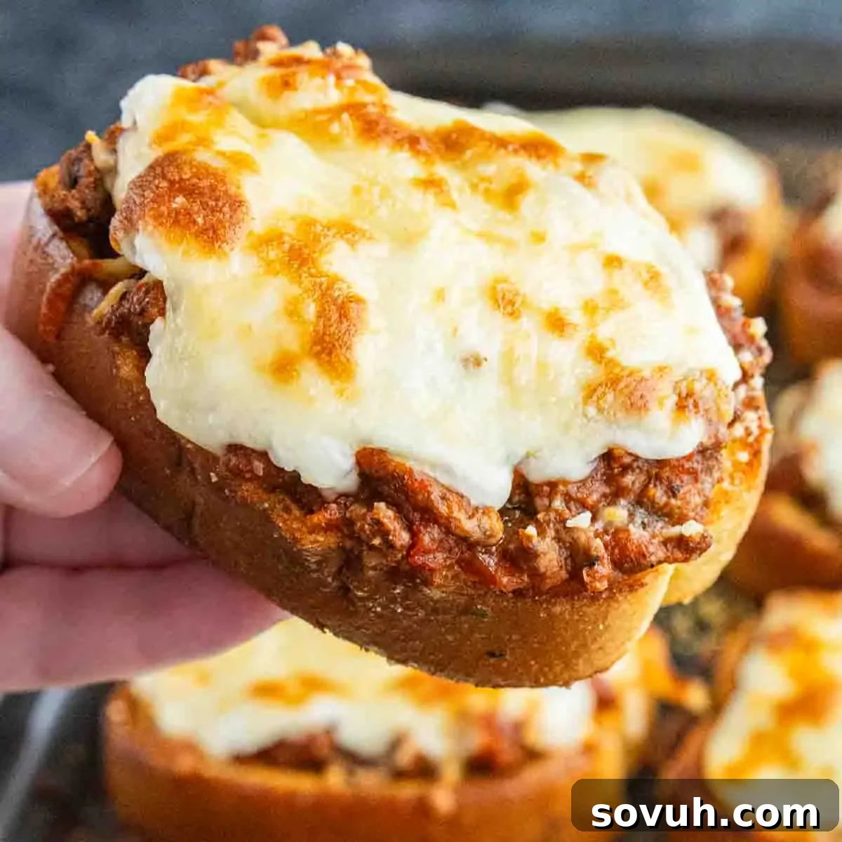 Texas Toast Garlic Bread Lasagna Recipe: Cheesy Weeknight Dinner 2 A hand holds a slice of easy garlic bread lasagna—seasoned ground beef, tomato sauce, and melted cheese atop thick bread; more slices are visible in the background.