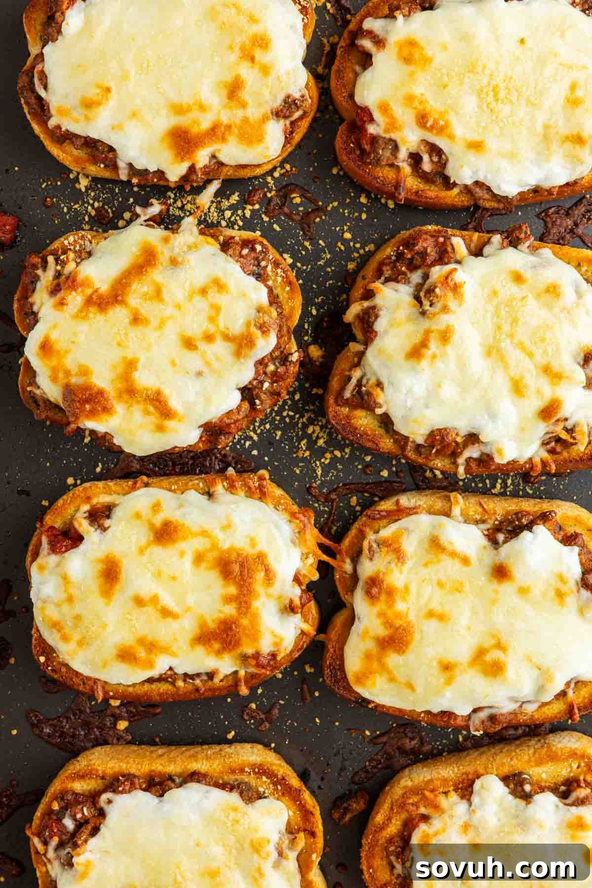 Texas Toast Garlic Bread Lasagna Recipe: Cheesy Weeknight Dinner 5 Nine pieces of toasted bread topped with meat sauce and melted, browned cheese are arranged on a dark baking sheet, creating an easy Garlic Bread Lasagna twist that's perfect for Texas Toast Lasagna fans.