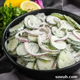 Creamy Summer Cucumber Salad with Dill and Yogurt 10 A black bowl filled with creamy cucumber salad made of cucumber and red onion slices in a dill dressing, with parsley and lemon in the background.