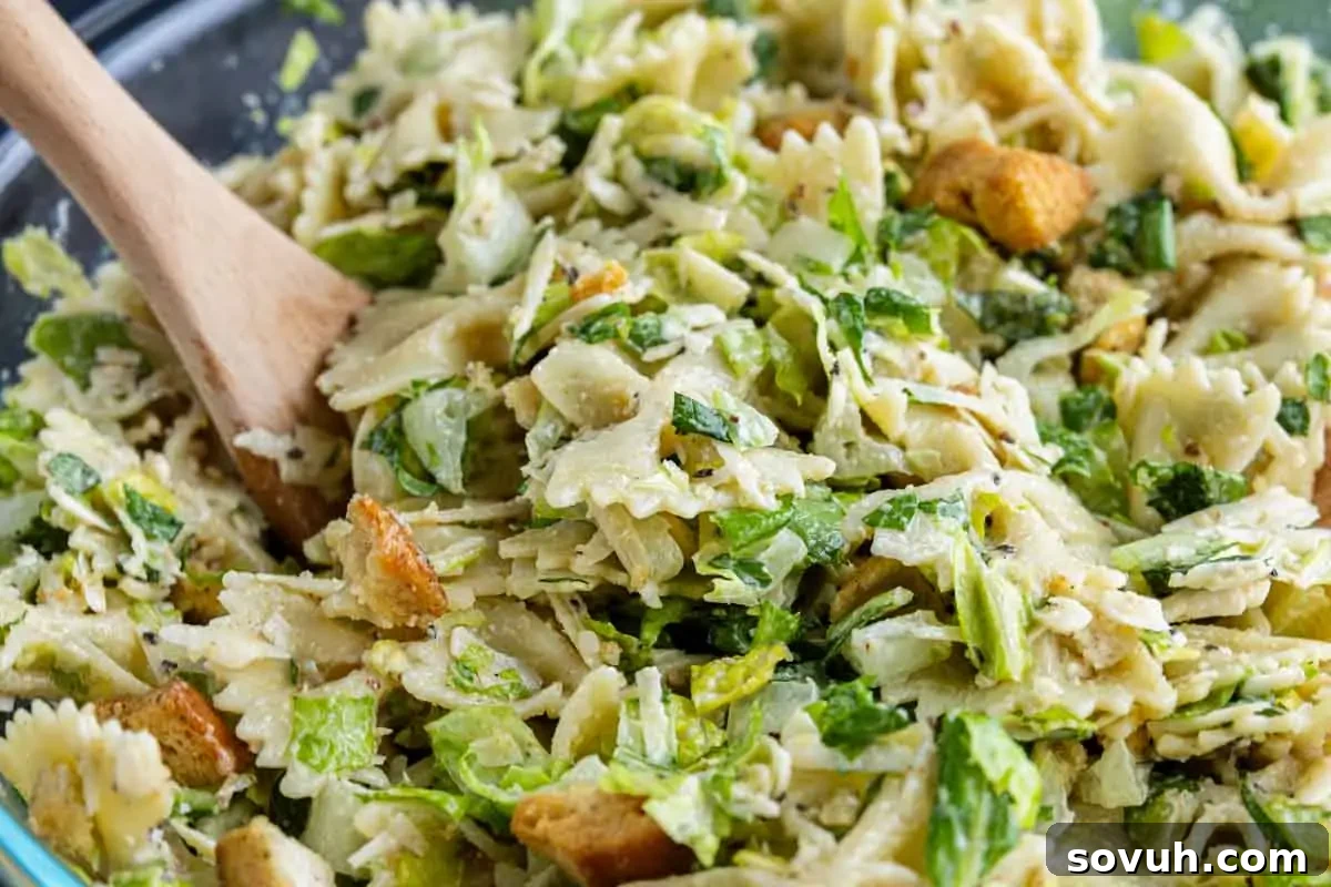 Creamy Caesar Pasta Salad Recipe for Summer Potlucks 2 A close-up of a cold pasta salad with bowtie pasta, chopped lettuce, croutons, and a creamy dressing, mixed in a bowl with a wooden spoon—a fresh twist on the classic Caesar salad pasta salad recipe.