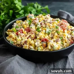 Southern Cornbread Salad Recipe for Potlucks and BBQs 7 A black bowl filled with Southern Cornbread Salad—mixed greens, cherry tomatoes, corn, green onions, and shredded cheese—set on a gray cloth with fresh herbs in the background; a perfect Southern potluck side dish.