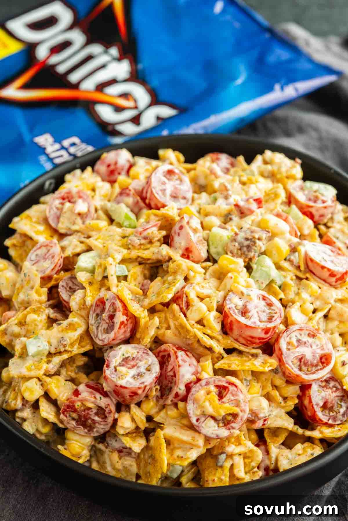 Crunchy Cool Ranch Doritos Salad with Bacon & Sweet Corn 5 A bowl of Cool Ranch Doritos Salad with chopped tomatoes, corn, green onions, and creamy dressing, with a bag of Doritos chips in the background.